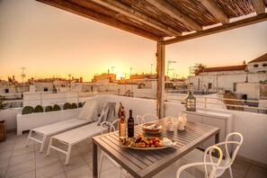 Eine Dachterrasse mit Esstisch, Stühlen, einer Couch und Blick auf die Skyline im Abendrot.