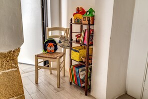 A wooden chair with a woven seat, a bookshelf with colorful books and toys, and a window with a view of the outside.