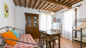A room with a bed, a wooden dining table with chairs, a cabinet, and a ceiling with exposed beams. - Bilo first floor terrace (Riparbella)