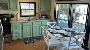 Une cuisine avec des meubles de couleur verte, un fourneau, un grille-pain et un coin repas avec des chaises et une table blanches.