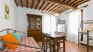 A bedroom with a bed, a wooden cabinet, a dining table with chairs, and a ceiling with exposed beams. - Bilo ground floor with garden (Riparbella)