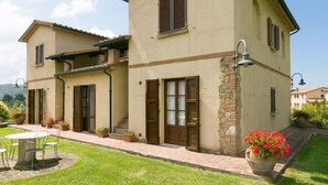 A two-story house with a patio, a dining table, and potted plants. - Bilo ground floor with garden (Riparbella)