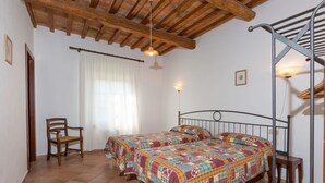 A bedroom with two beds, a chair, a wooden ceiling, and a window with curtains. - Bilo ground floor with garden (Riparbella)