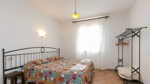 A bedroom with a bed, a bedside table, a hanging clothes rack, and a window with curtains. - Trilo standard first floor (Riparbella)