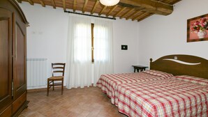 A bedroom with a wooden bed, a chair, a radiator, and a ceiling fan. - Bilocali Superior first floor terrace (Riparbella)