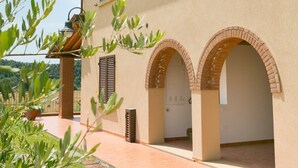 A building with a tiled roof, arched doorways, and a paved walkway. - Bilocali Superior first floor terrace (Riparbella)