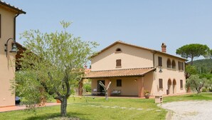 A two-story house with a tiled roof, a covered porch, and a small garden with a tree. - Trilo Superior ground floor (Riparbella)