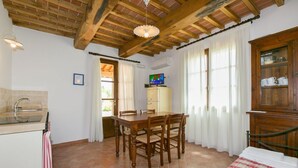 A room with a wooden dining table, chairs, a bed, a cabinet with dishes, and a television. - Trilo Superior ground floor (Riparbella)