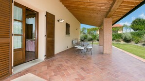 An outdoor patio with a tiled floor, a wooden pergola, and a table with chairs. - Trilo Superior ground floor (Riparbella)