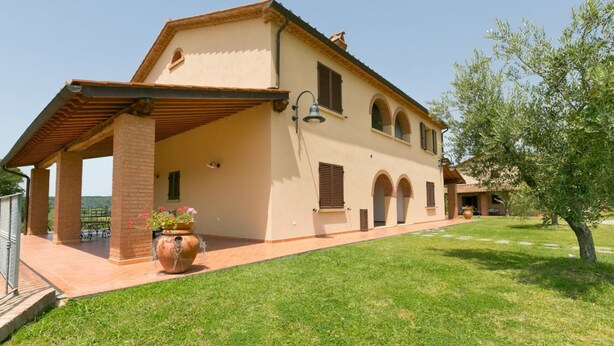 A two-story house with a covered patio, a large potted plant, and a well-maintained lawn. - Trilo Superior ground floor (Riparbella)