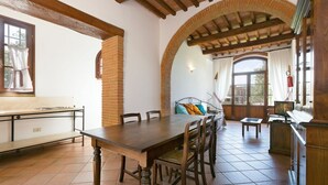Un comedor con una mesa y sillas de madera, un banco y vistas a través de un arco.