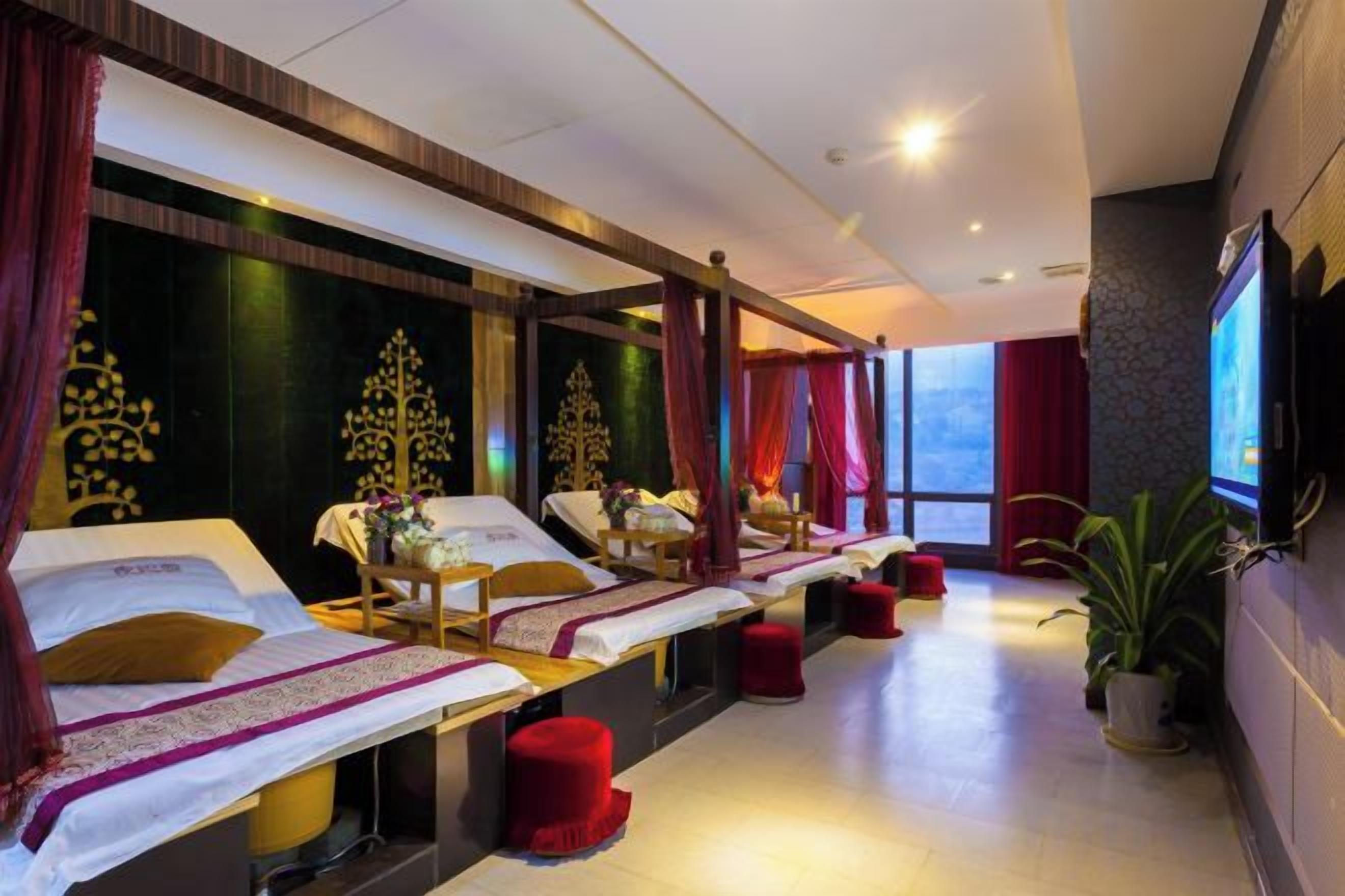A spa room with multiple beds, red cushions, and a large window providing natural light.