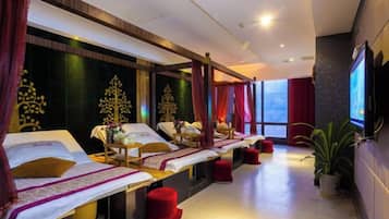 A spa room with multiple beds, red cushions, and a large window providing natural light.