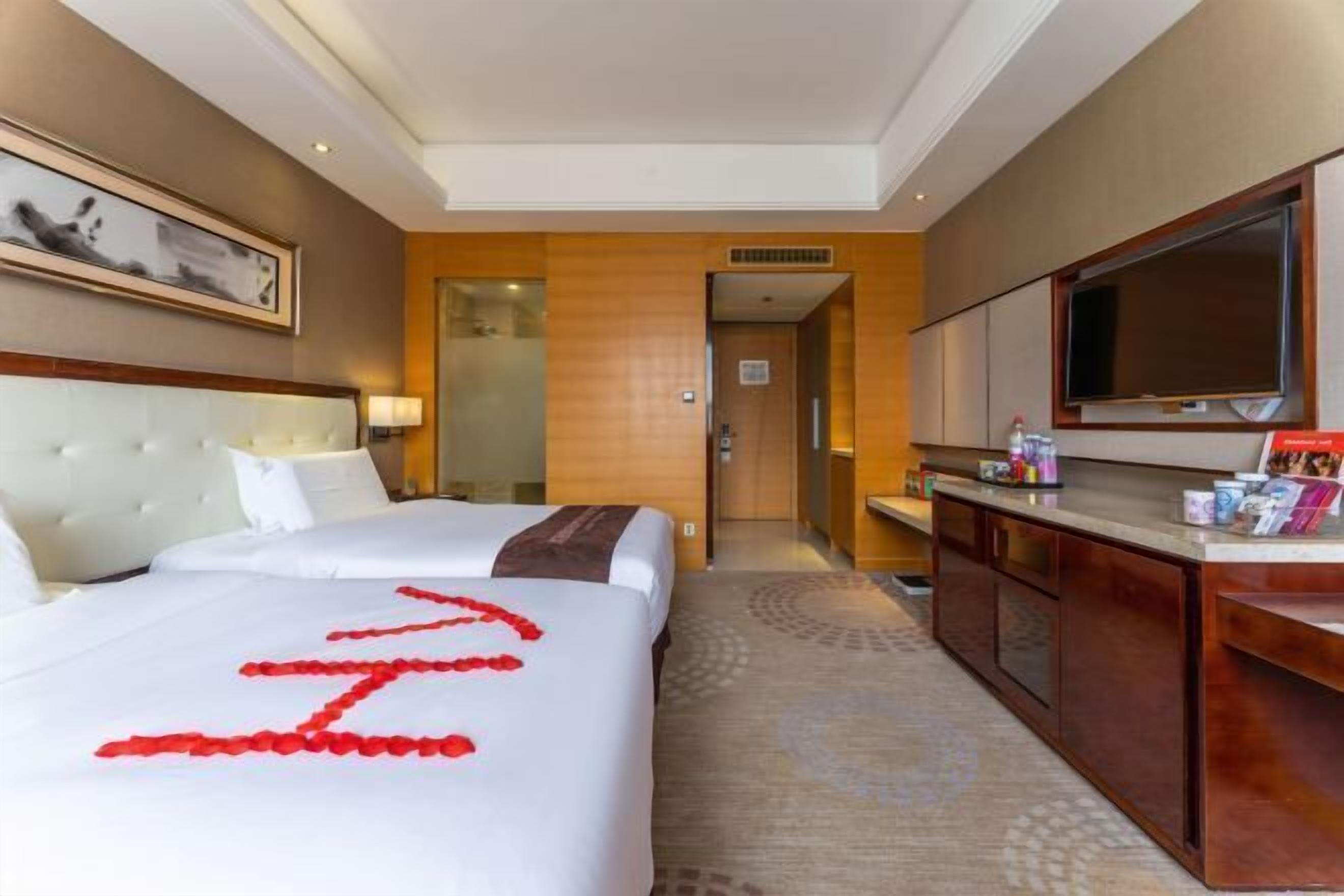 A hotel room with a large bed, a TV, a desk, and a bathroom visible through an open door.
