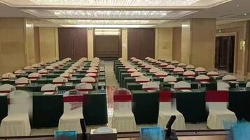 Un salón de conferencias con filas de mesas y sillas, una araña y un espejo grande.