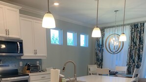 A modern kitchen with a large island, bar stools, and pendant lighting. -  SINGLE FAMILY HOME IN DESIRABLE NAPLES RESERVE (Naples)