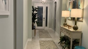 A hallway with a patterned rug, a console table with lamps, and a door at the end. -  SINGLE FAMILY HOME IN DESIRABLE NAPLES RESERVE (Naples)