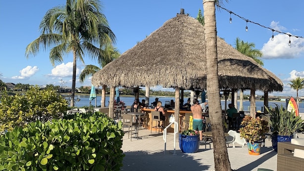 A beachside bar with outdoor seating, palm trees, and a thatched-roof structure. -  SINGLE FAMILY HOME IN DESIRABLE NAPLES RESERVE (Naples)