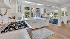 A spacious kitchen with white cabinetry, a gas stove, and a large window overlooking a garden. - A Slice of Heaven near Rancho Santa Fe (Del Mar)