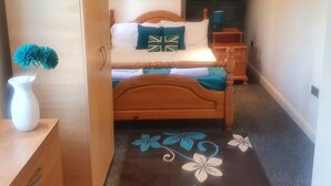 A bedroom with a wooden bed, a nightstand, a dresser, and a floral-patterned rug.