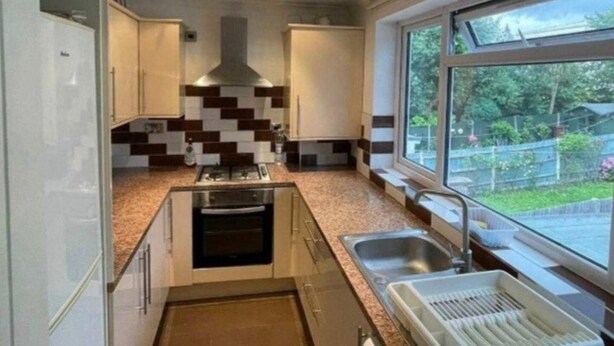 A modern kitchen with a central island, a built-in oven, a stainless steel sink, and a window with a view of greenery.