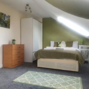 A bedroom with a bed, a dresser, a nightstand, and a green accent wall. - Lovely 4-bed Apartment in Harrow (Harrow)