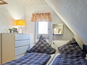 A bedroom with two beds, a dresser, a lamp, a window with a curtain, and a wall-mounted mirror.