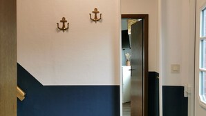 Un pasillo con pared blanca y azul marino, un marco de puerta de madera y un espejo que refleja una zona de cocina.