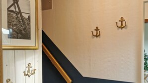 Una escalera con barandilla de madera, pared blanca con textura y tres anclajes de bronce.