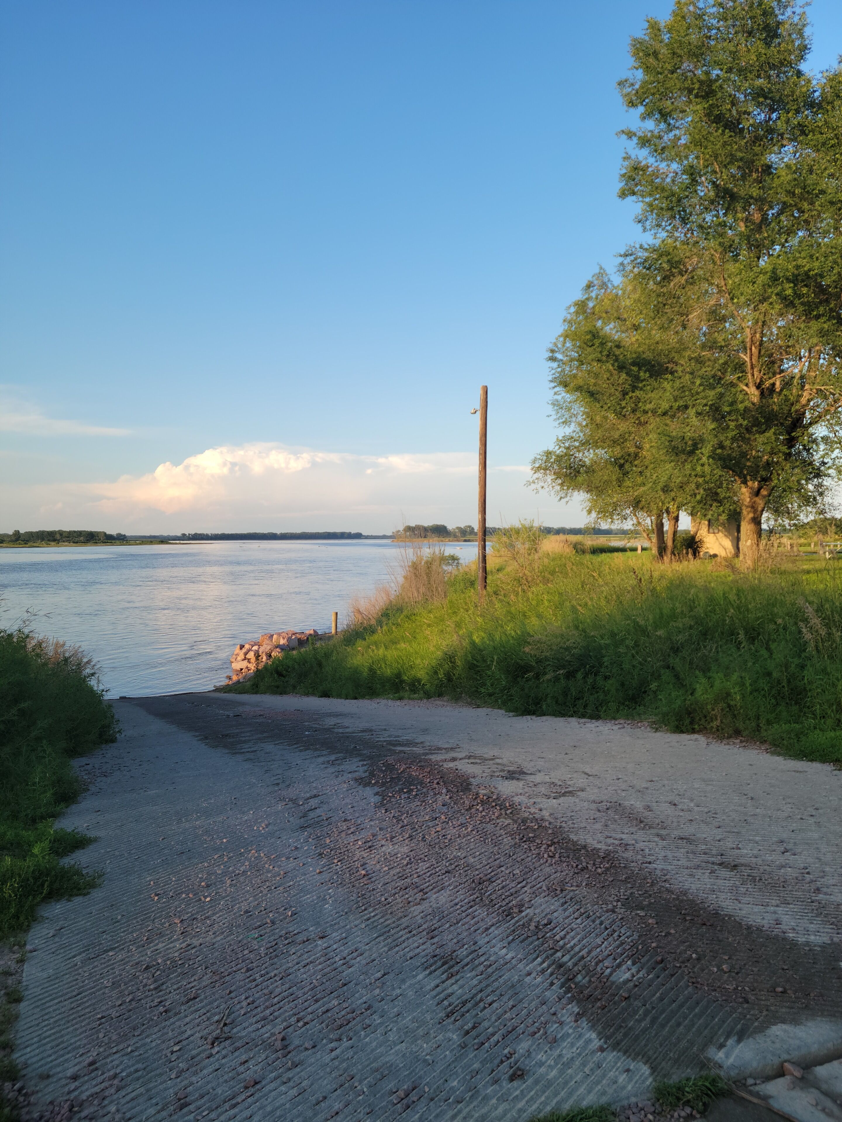 A gravel path leading to a body of water, surrounded by greenery and a clear sky.