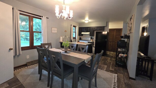 A dining area with a table, chairs, and a chandelier. There is a kitchen in the background with appliances and cabinets. - Cozy Get away.   (Newcastle)