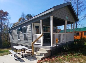 A two-story house with a porch, a small table, and steps leading to the entrance. - 104) Falcon Farmhouse Style Cabin. Close to Hocking Hills State Park and more! (Logan)