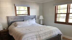 A bedroom with a large bed, wooden headboard, two bedside tables with lamps, and a patterned rug.