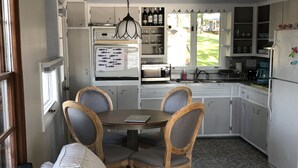 A compact kitchen with white cabinets, a dining table with chairs, and a window overlooking a yard.