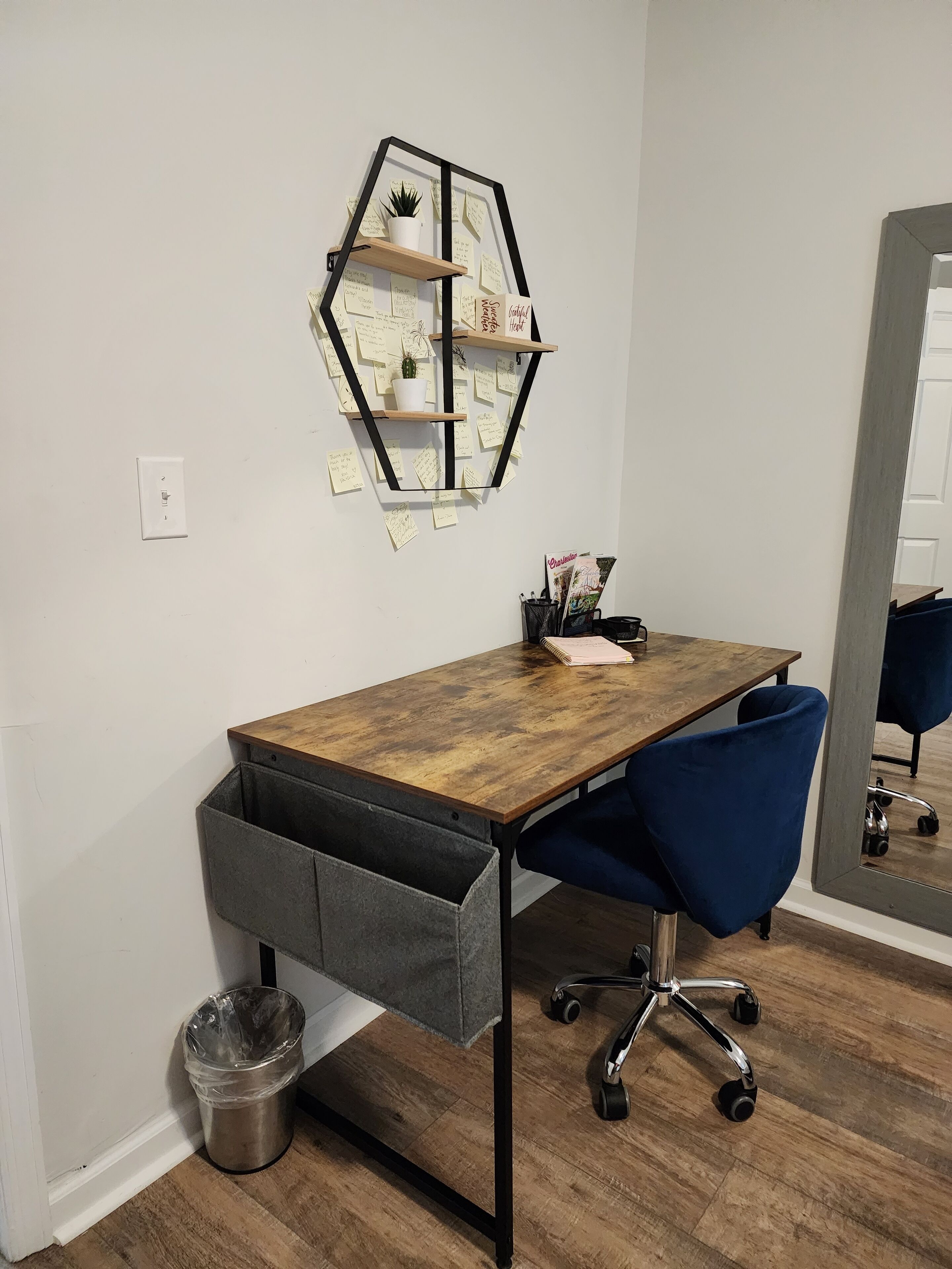 A wooden desk with a hexagonal shelf, a blue office chair, and a trash can.