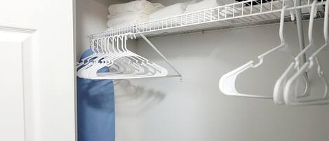Un placard avec des cintres blancs et un sac bleu.