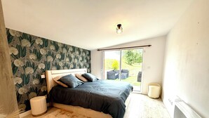 Ein Schlafzimmer mit einem Bett, einem Nachttisch, einem flauschigen Teppich, einer Wand mit Blumenmuster und einer Glastür, die zu einem Außenbereich führt.