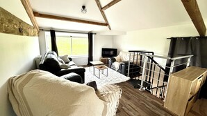 Ein Loft-Zimmer mit Holzboden, einer Couch, einem Sessel, einem Fernseher und einer Treppe.