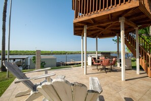 Un patio techado al aire libre con vista a un lago, sillas de madera y zona de barbacoa.