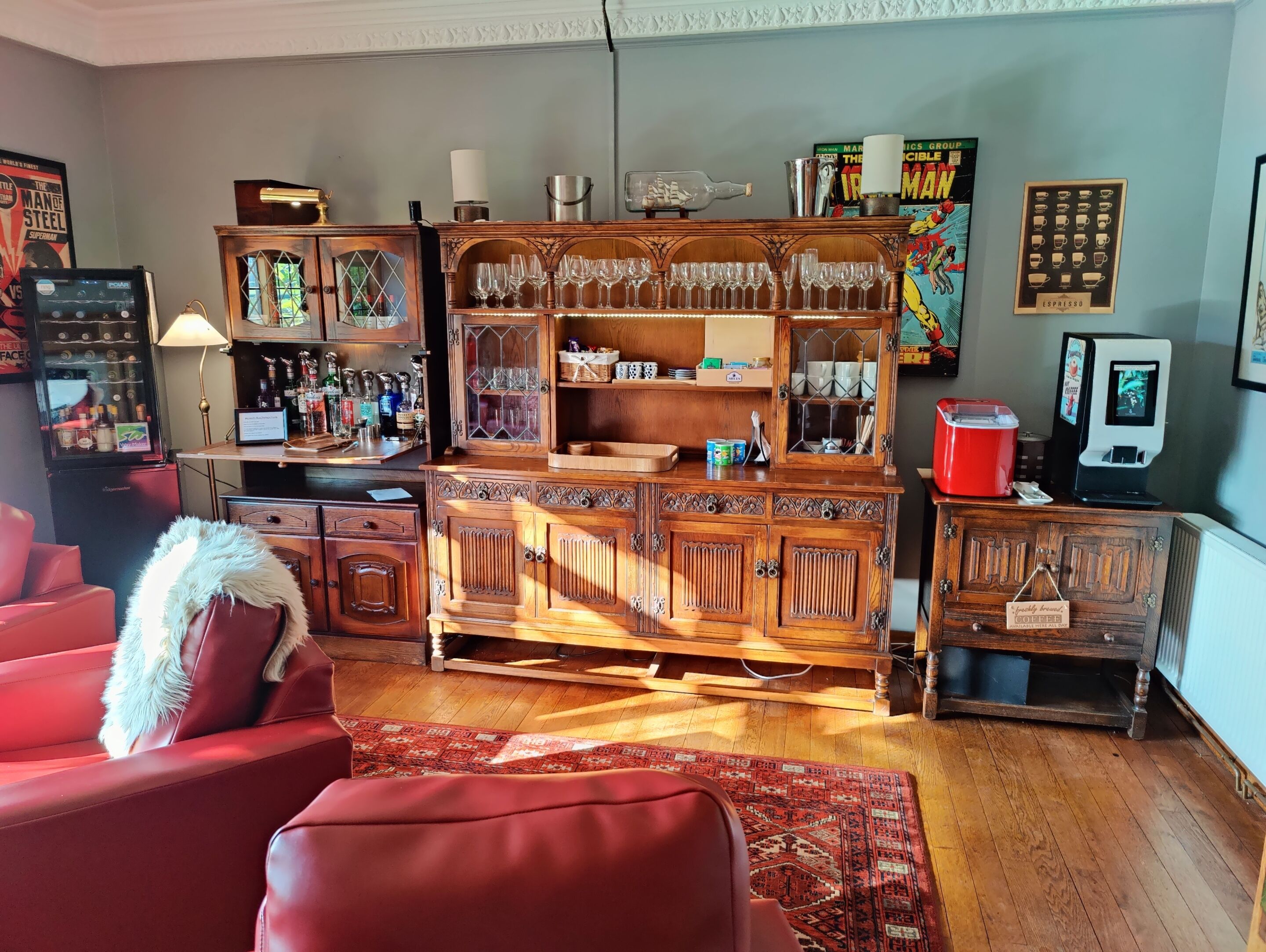 A cozy living room with a red sofa, wooden cabinets with glass doors, a coffee machine, and a world map on the wall.