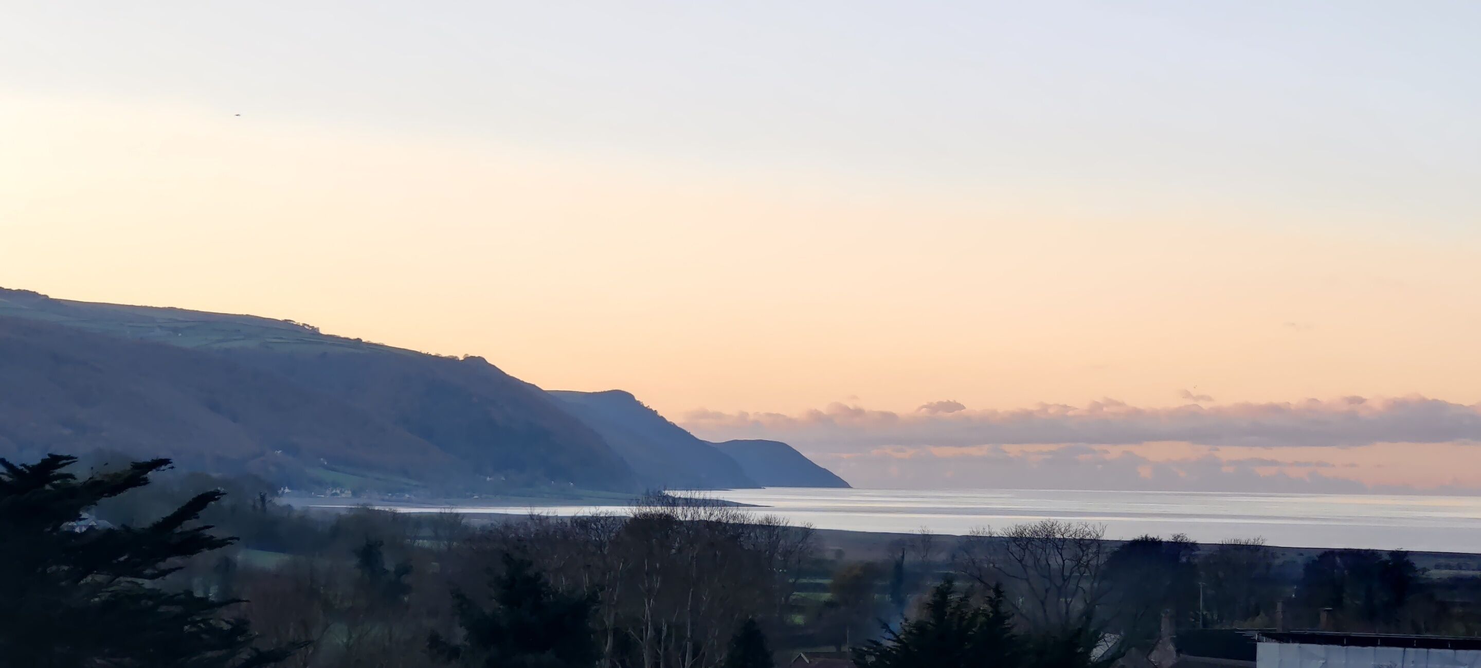 A coastal landscape with a view of the sea and distant mountains.