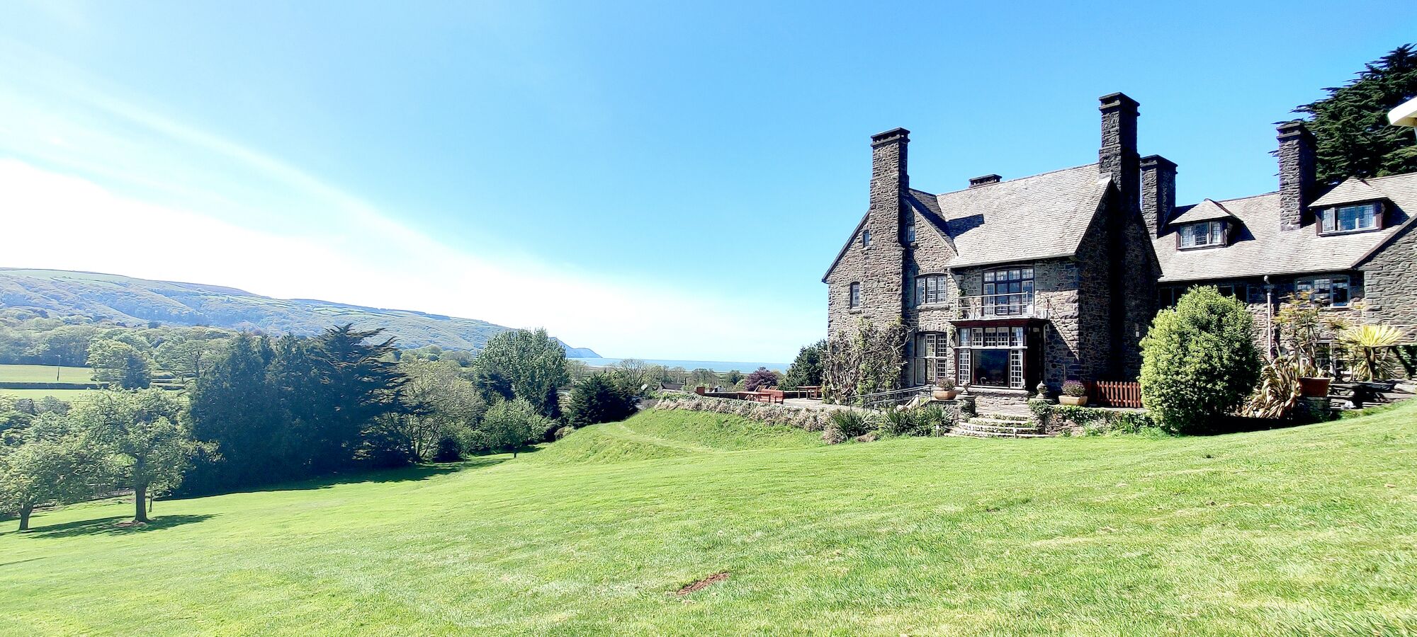A large stone house with a prominent chimney, surrounded by a well-maintained lawn and trees.