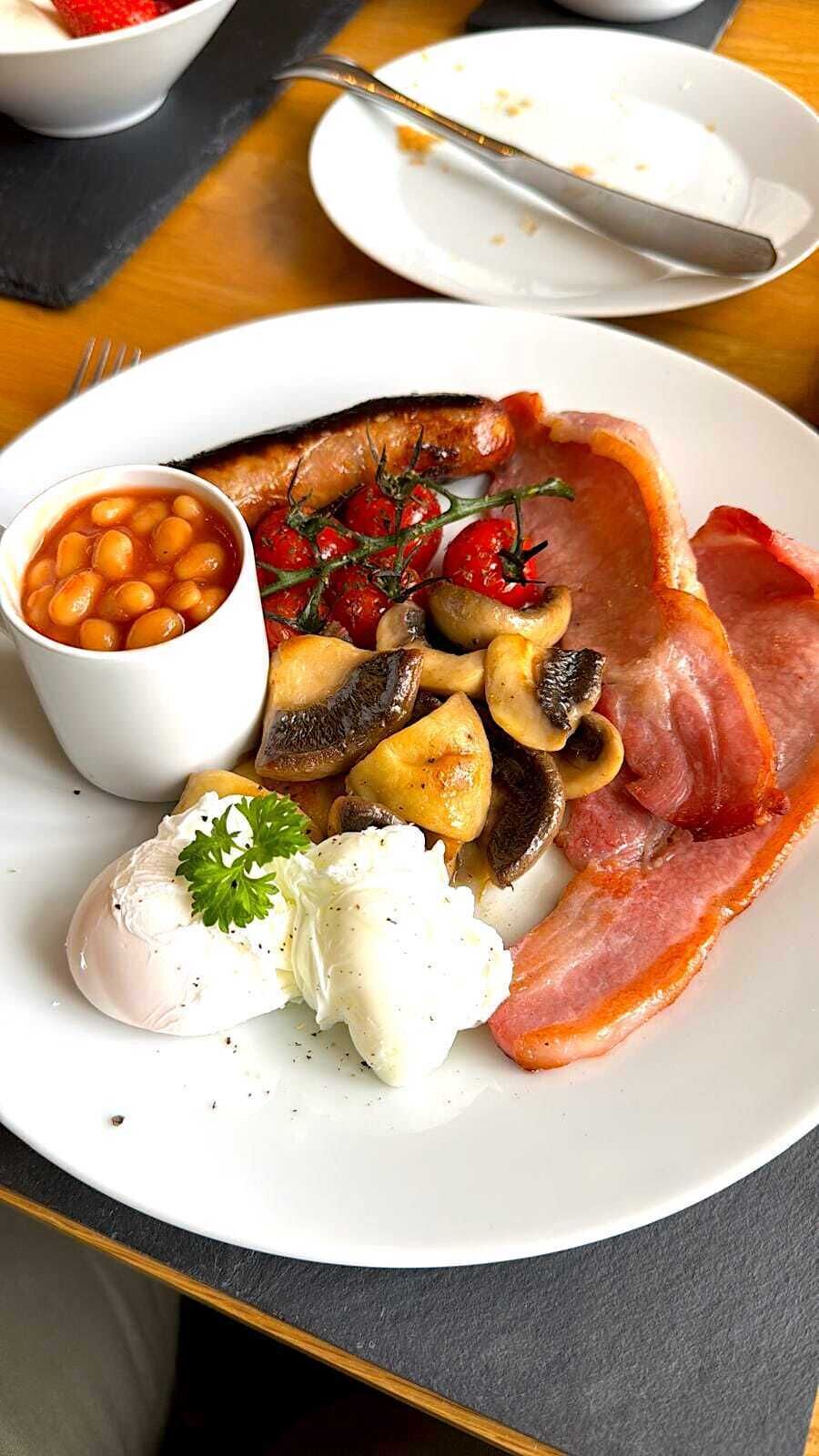 A plate of food with beans, mushrooms, bacon, and a poached egg.
