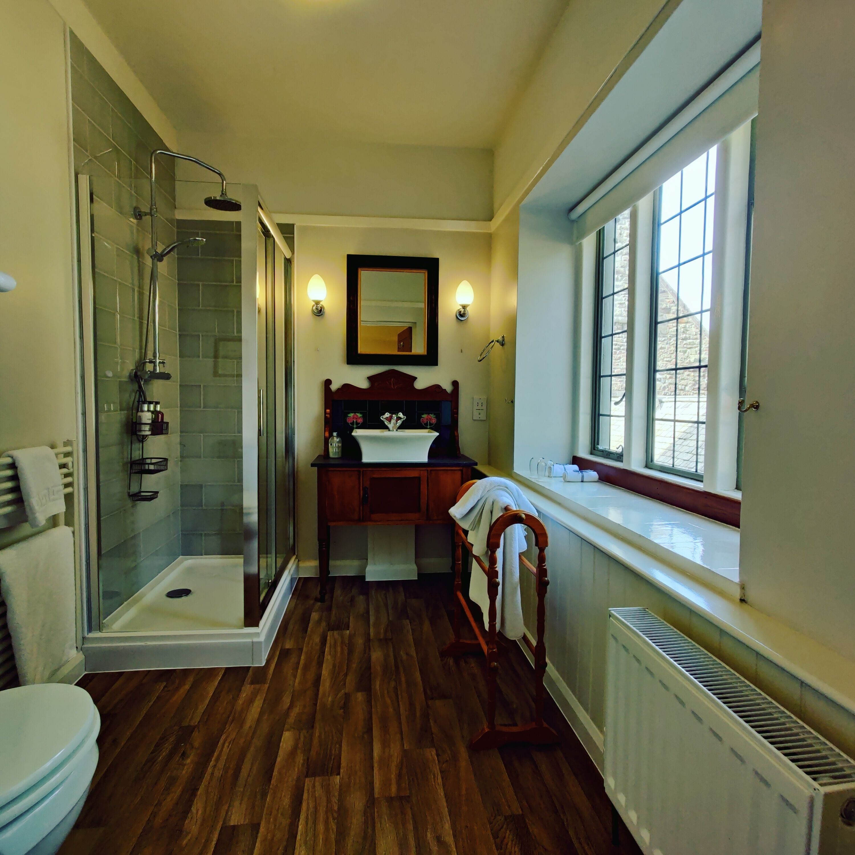 A bathroom with a glass-enclosed shower, a wooden vanity, a mirror, and a window providing natural light.
