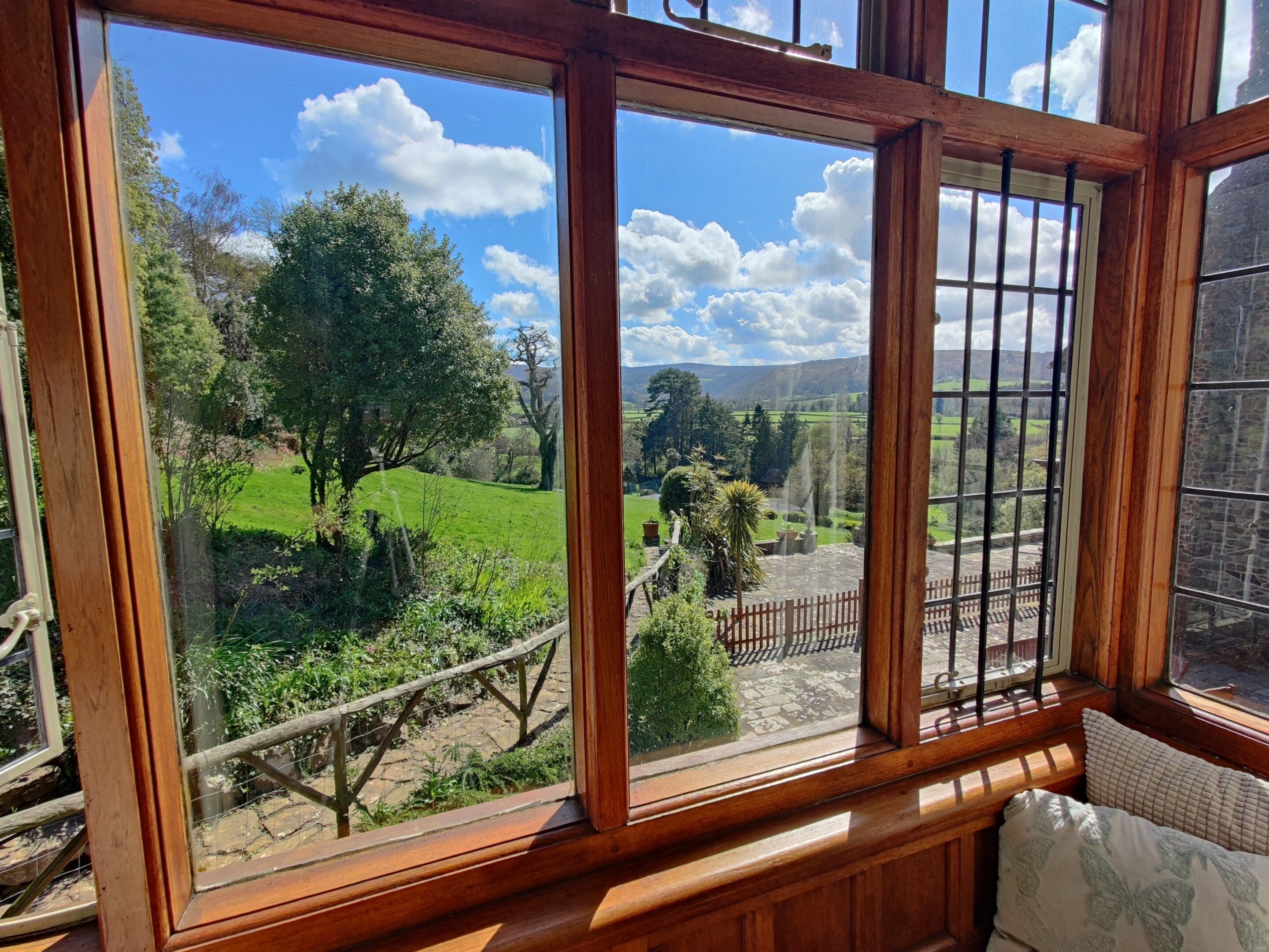 A room with a large window offering a view of a green landscape with trees and a stone wall.