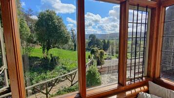 A room with a large window offering a view of a green landscape with trees and a stone wall.
