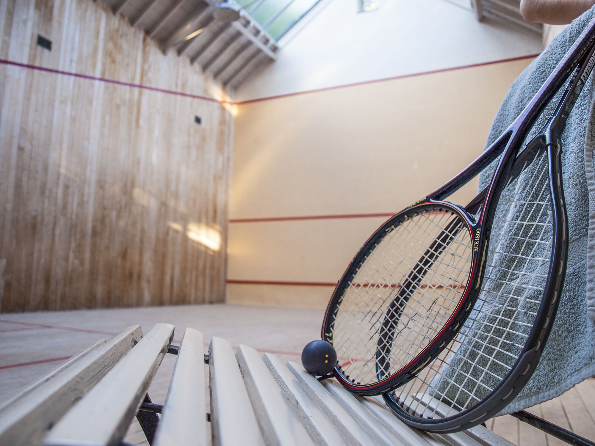 A squash court with a wooden floor, a metal barrier, and a towel on a bench.
