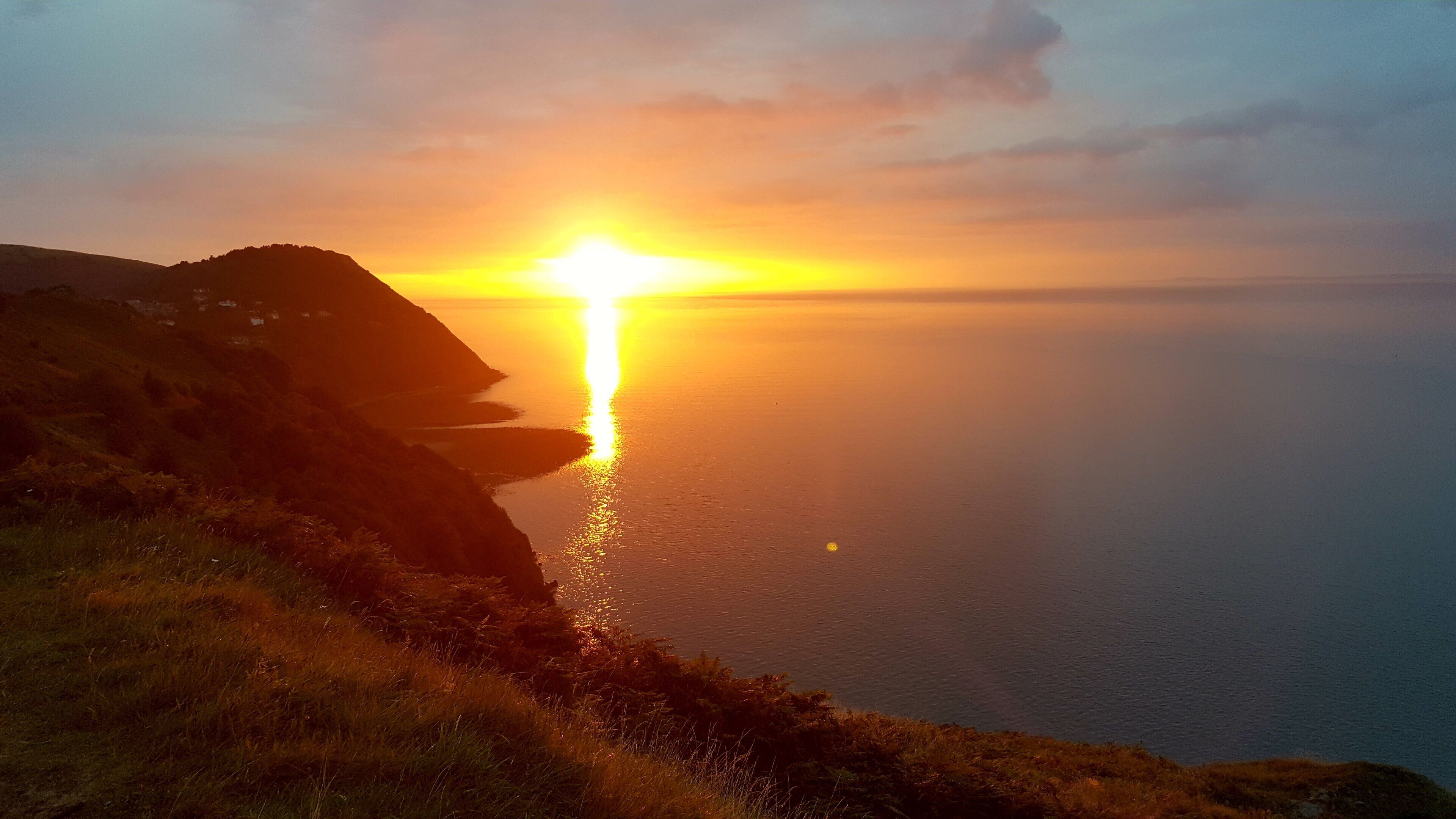 A coastal sunset with a clear view of the sea and a grassy cliff.