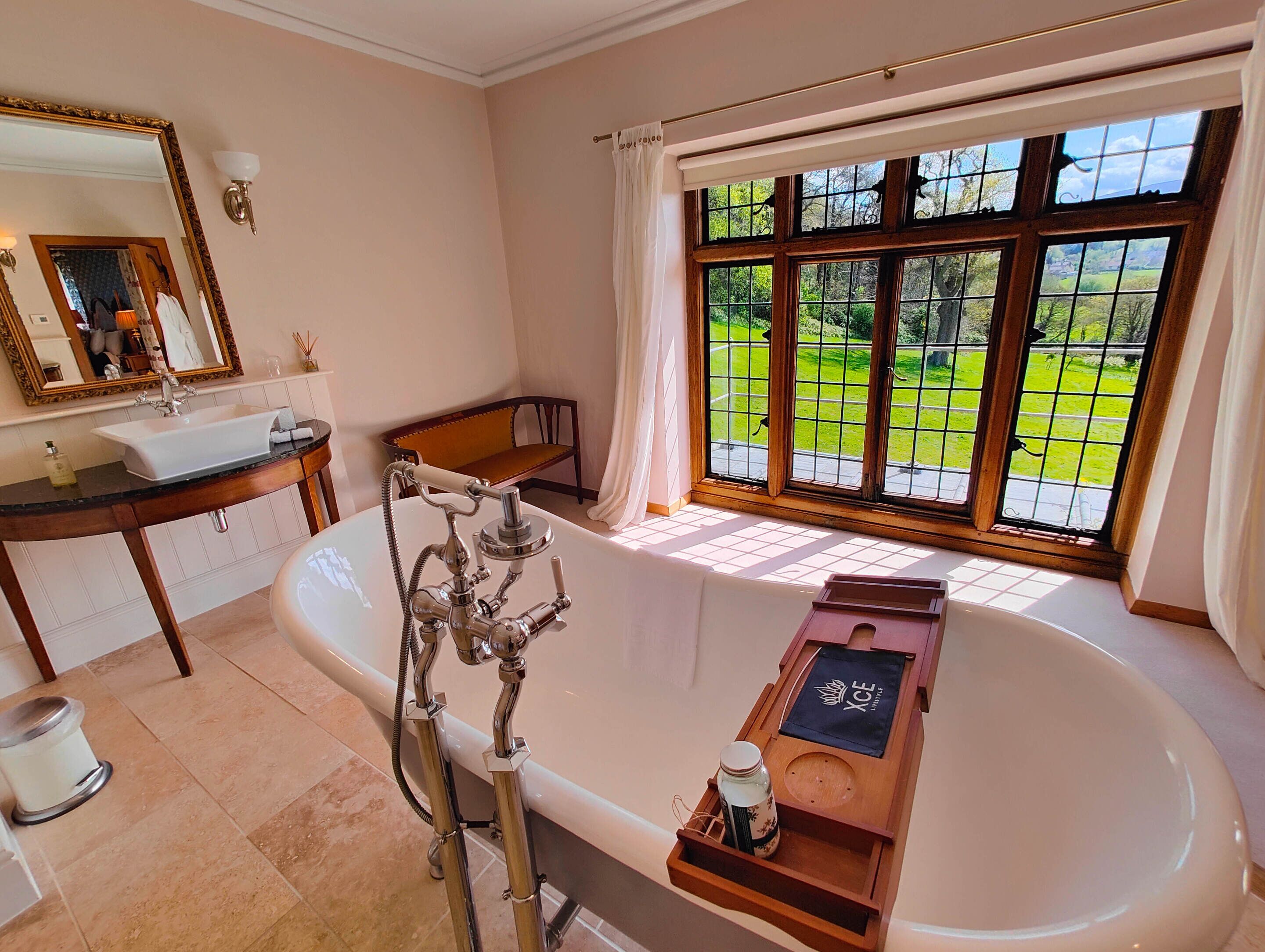 Un baño con bañera, tocador con espejo y ventana con vistas a la vegetación.