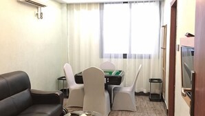 A hotel room with a sofa, a table with a board game, a TV, and a window with curtains. - Xindeli Apartment (Lufeng)